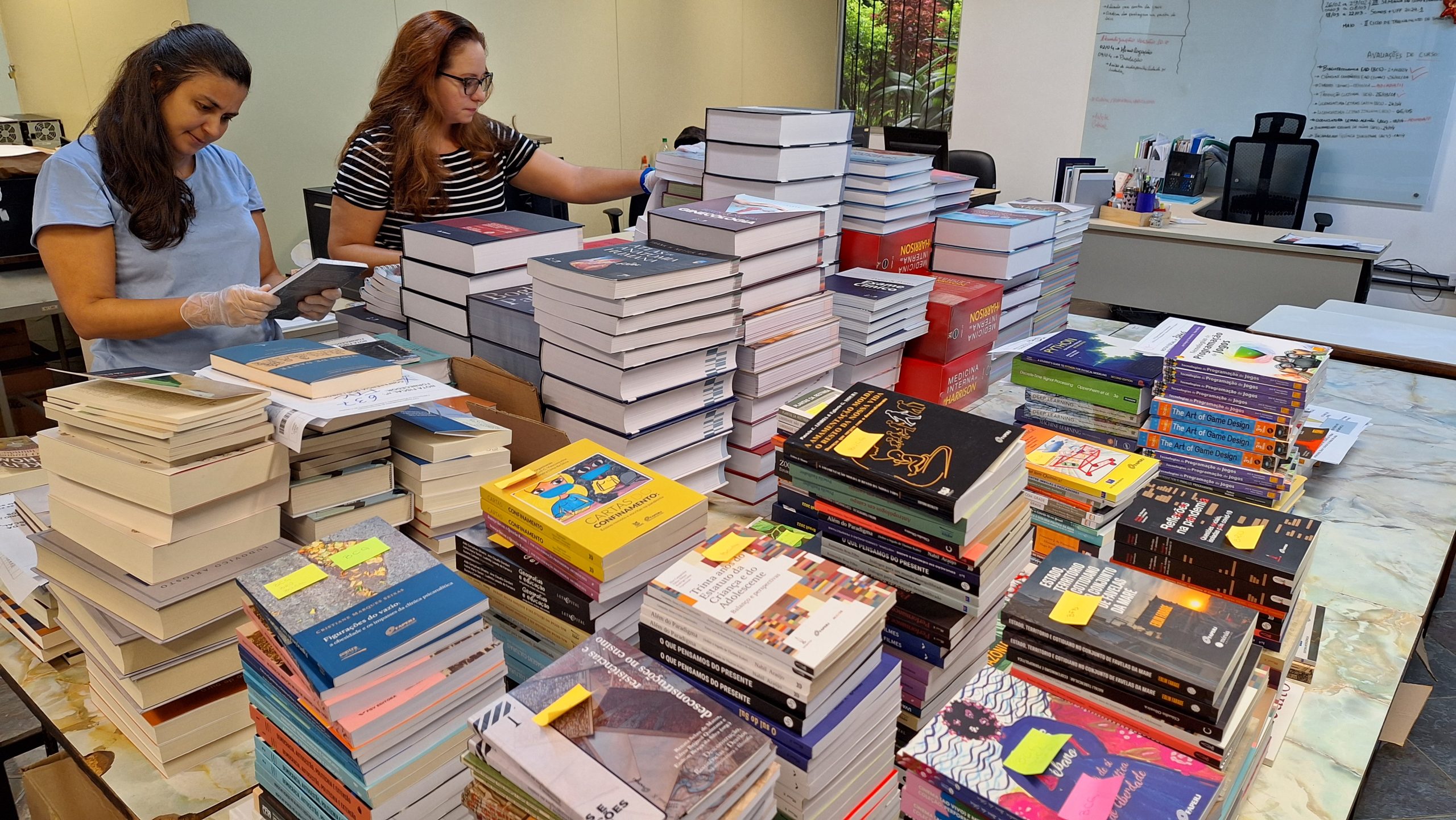Servidoras Brunna Mathias e Mônica da Costa organizando os livros para distribuição Servidoras Brunna Mathias e Mônica da Costa organizando os livros para distribuição